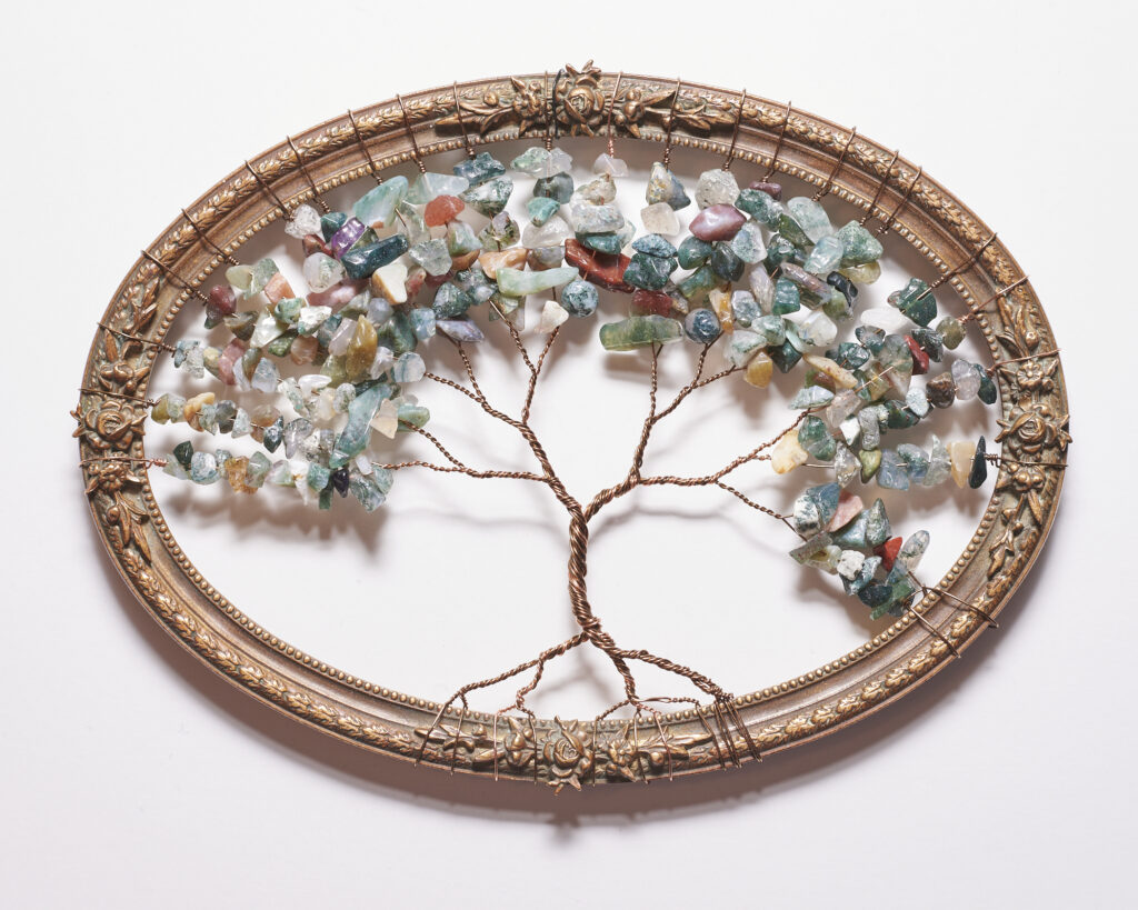 A picture of a wire Tree of Life sculpture in an antique oval frame. The tree is made from wire in various copper/brown colours. The leaves are multicoloured semi precious stones. The oval frame is antique bronze with little rosettes decorating the outside of it.