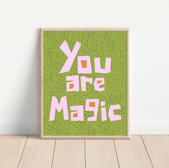 Framed art print with encouraging message "You Are Magic" in hand drawn block letters. The frame is sitting on a wooden floor and propped against a while wall.