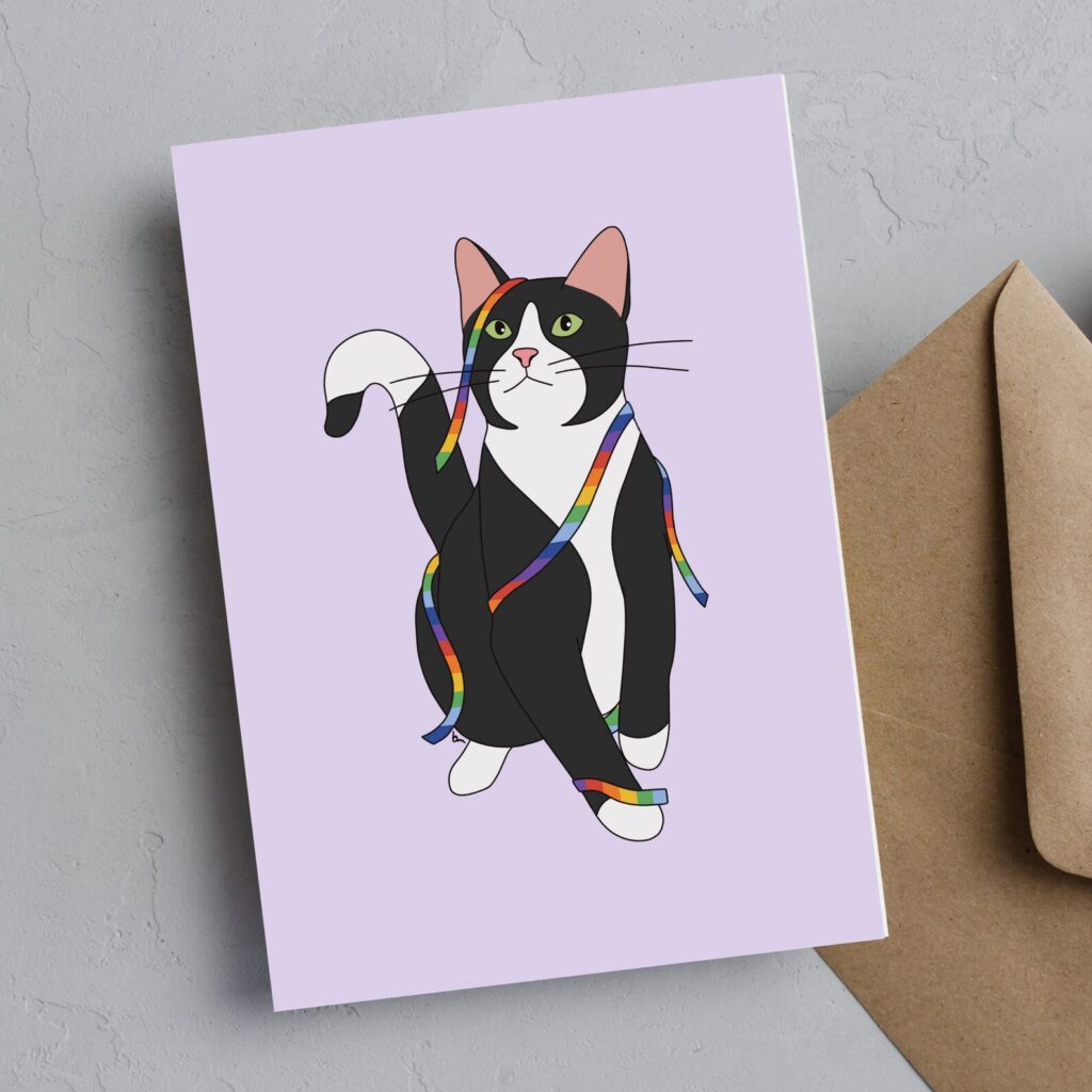 Greeting card and envelope. Greeting card features an illustration of a black and white tuxedo cat with green eyes, tangled in a rainbow ribbon, against a light purple background.