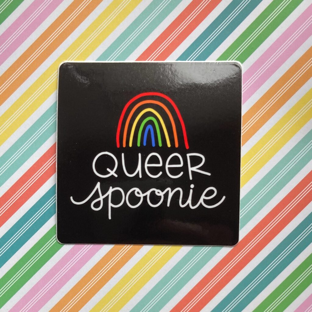 A square black sticker with rounded corners that has white hand lettering reading “queer spoonie” on it. There is a rainbow doodle above the lettering and the sticker is against a rainbow background.
